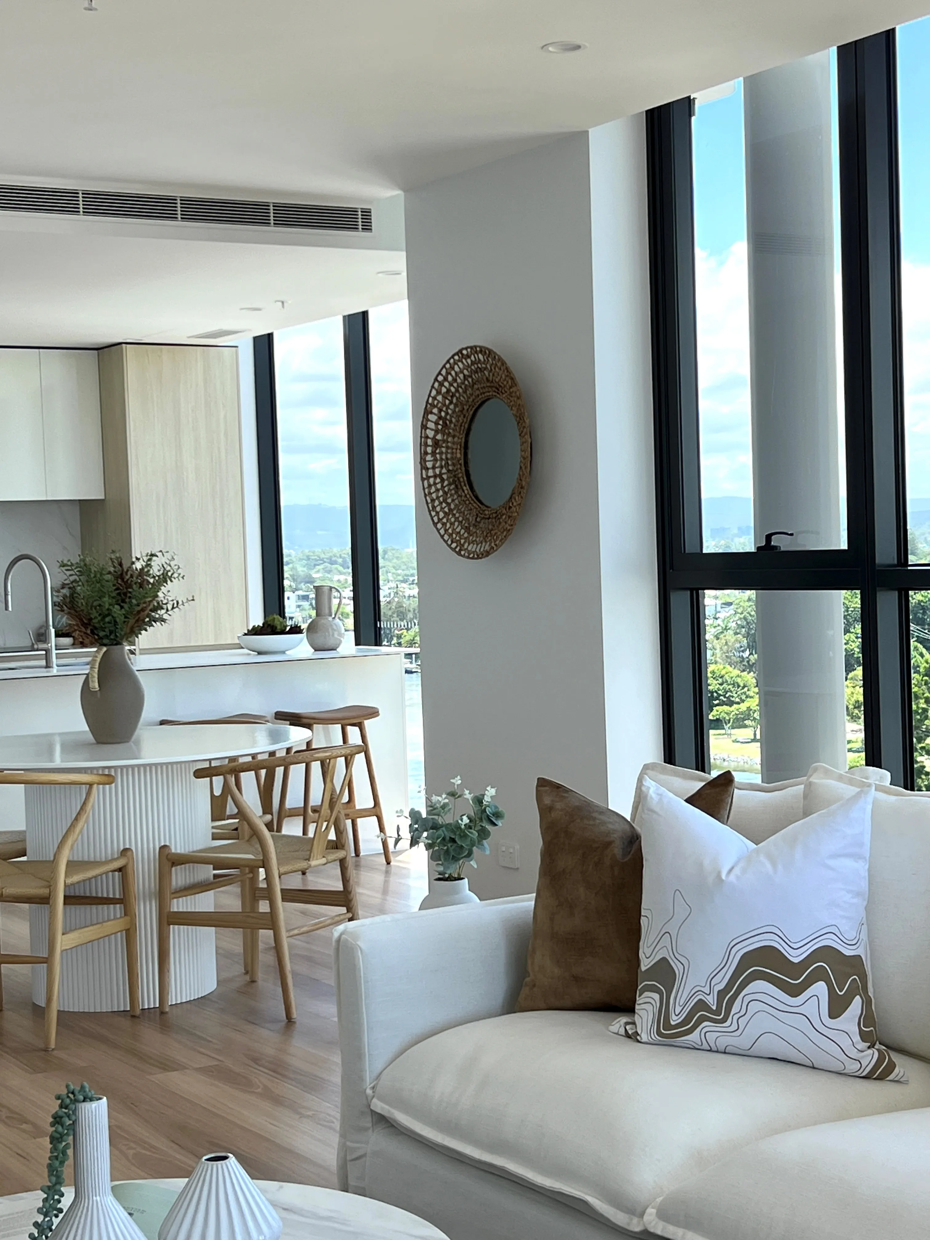 Open-plan living with cream sofa, woven round mirror, fluted kitchen island and hinterland views
